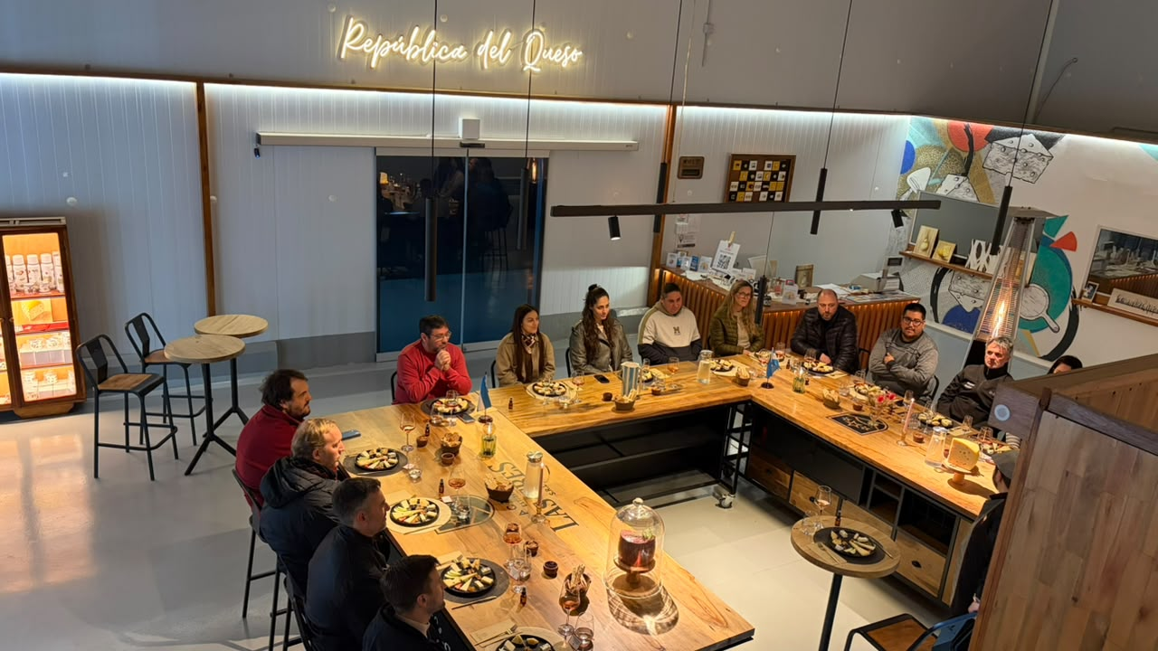 Asistentes sentados alrededor de una mesa preparada con platos de quesos y copas.